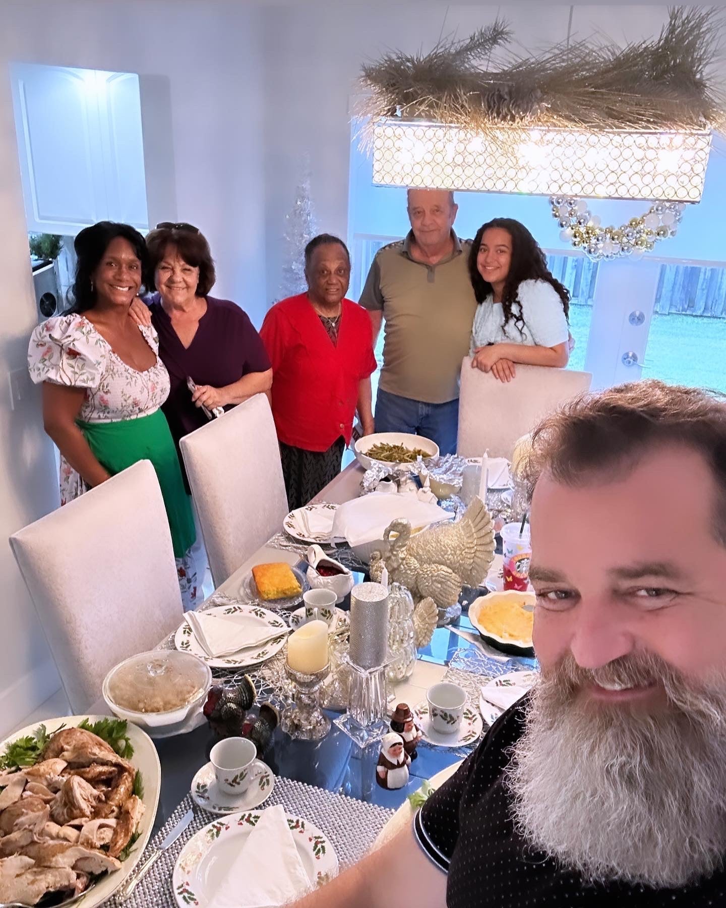 Family gathered around a beautifully set holiday dinner table, smiling and posing together in a festive dining room with Christmas décor.
